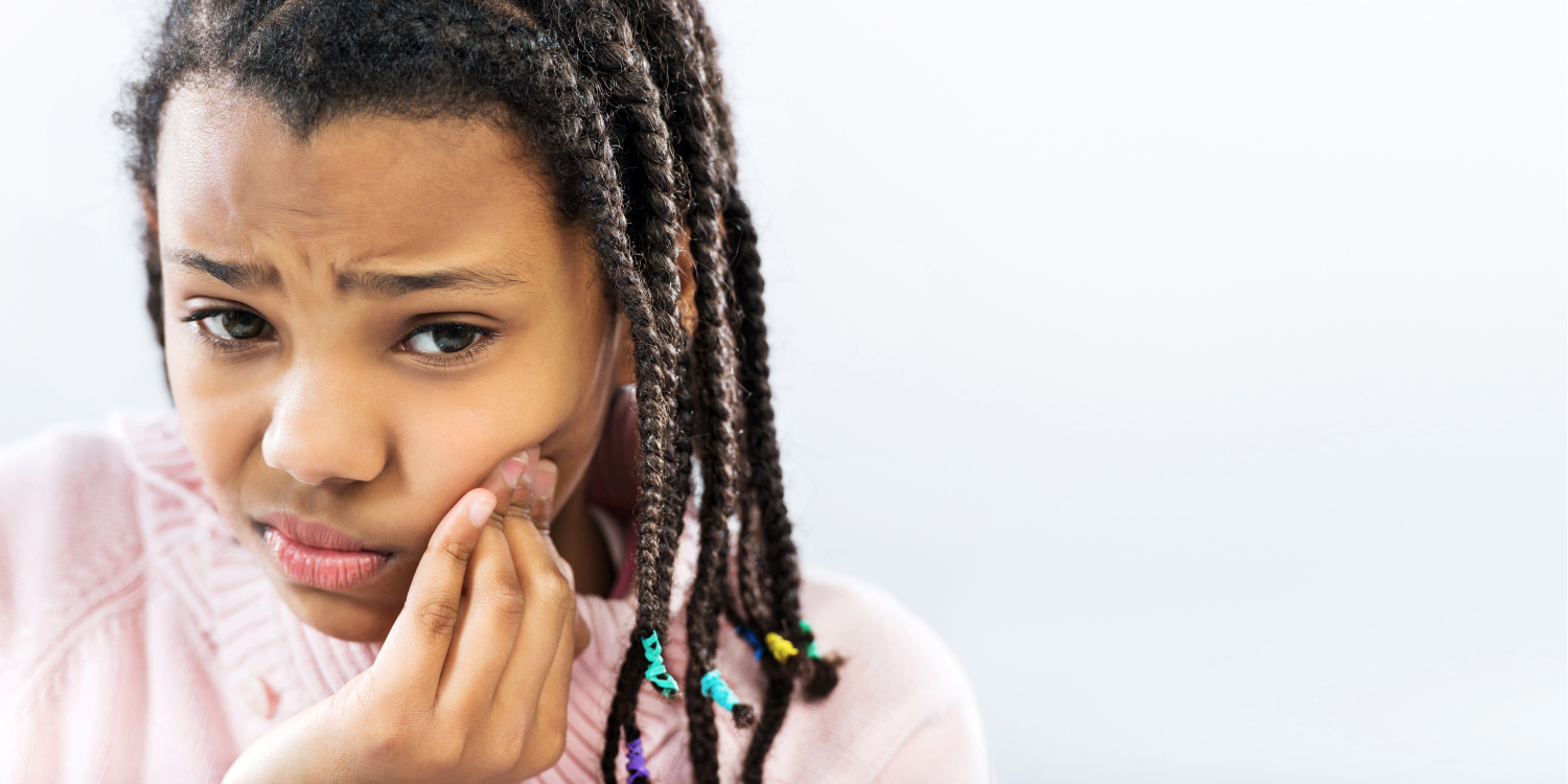 Young girl with braces cringes and touches her cheek because of an orthodontic emergency