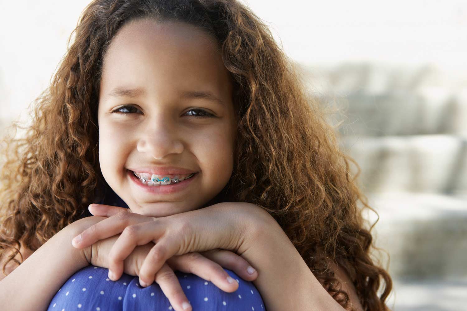 Brunette girl with early orthodontics smiles with her chin on her knees